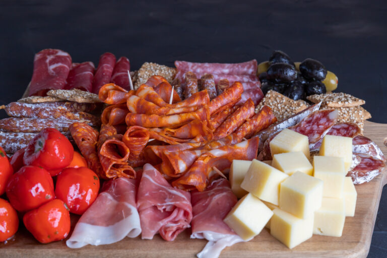 Cutting board with ham, salami, cheese, cracker and olives on a wooden board, close up, selective focus