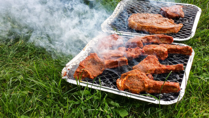 Lamb chops and Steak being grilled on a disposable grill in the park.