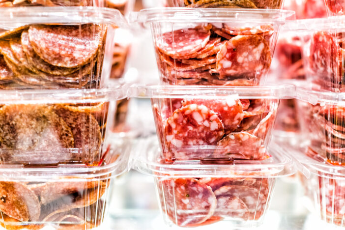 Closeup of sopressata and genoa salami cut many slices in plastic boxes containers stack pile on shelf display in a market shop butcher