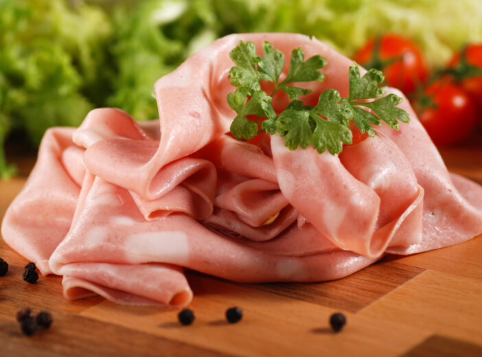 sliced mortadella on wooden chopping board with vegetables on the background