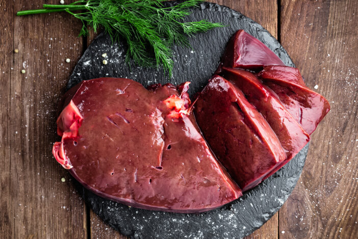 Raw liver on slate board on wooden background top view