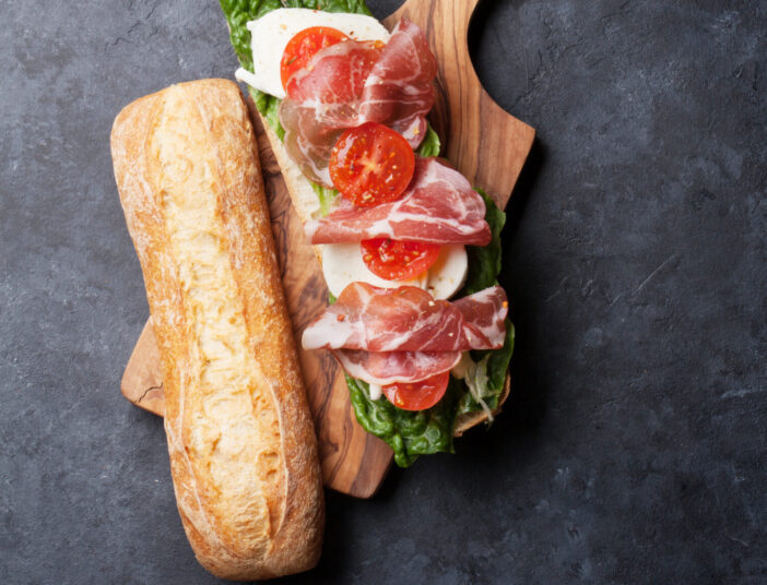 Ciabatta sandwich with romaine salad, prosciutto and mozzarella cheese on stone table. Top view with copy space