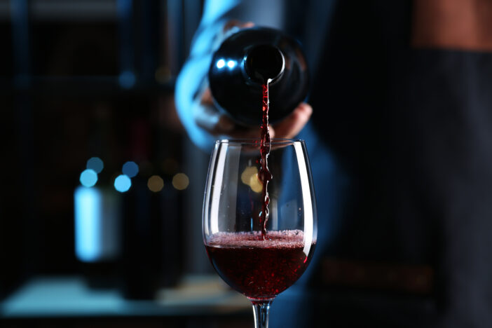 Bartender pouring red wine from bottle into glass indoors, closeup