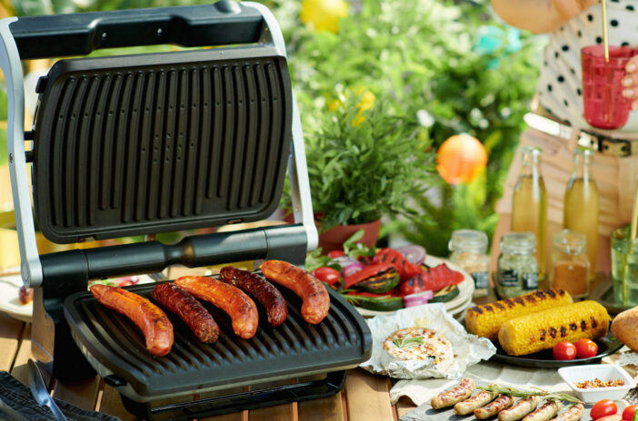 Summer backyard picnic. desk with electric grill and grilled sausages.