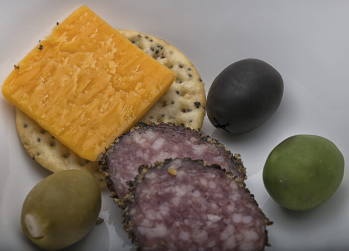 selection of cheddar cheese,peppered hard salami, a sesame cracker and three colorful olives