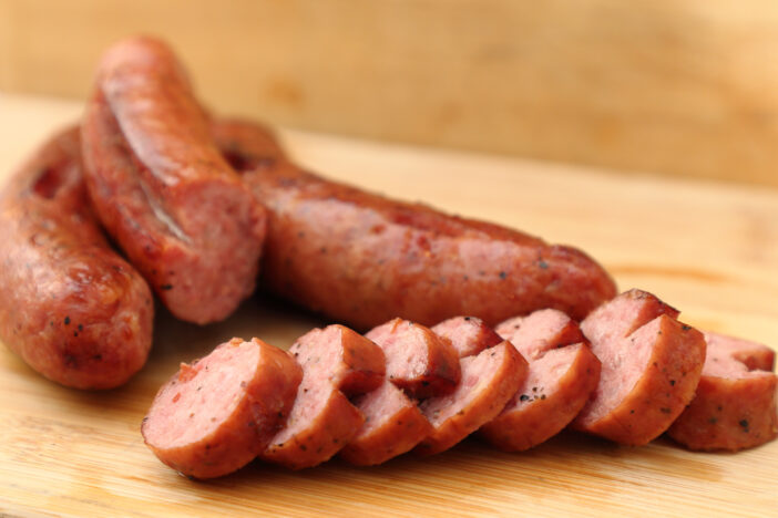 A picture of the smoked sausage sliced on the wooden table. The front row of sausage slices are in-focus.