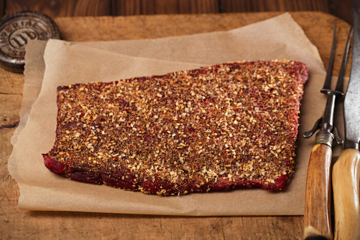 spice rubbed raw beef fillet, making jerky meat on wooden backdrop with vintage curving fork and knife