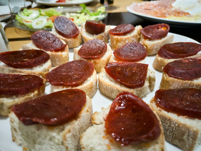 Simple plate of sliced bread with a piece of spicy red chorizo on top of the bread