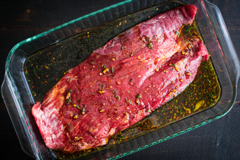 A raw flank steak marinating in a glass baking dish