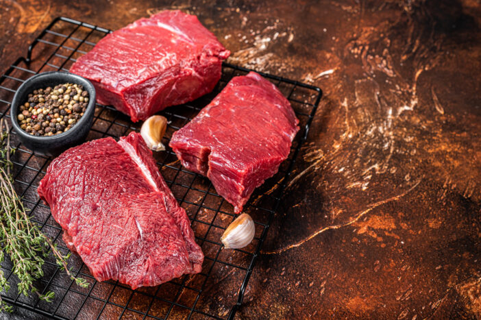Raw Wild Game Meat of  Venison dear ready for cooking. Dark background. Top view. Copy space.
