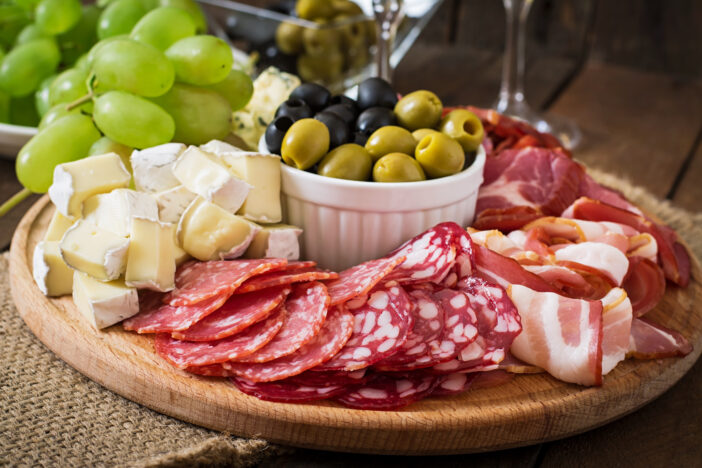 Antipasto catering platter with bacon, jerky, salami, cheese and grapes on a wooden background