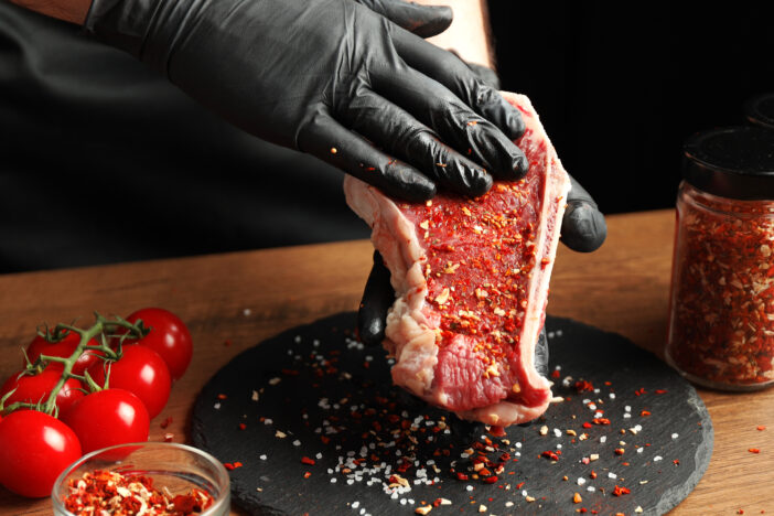 Beef steak with spices in the hands of the cook on a black background.