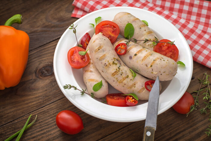 Boiled grilled sausages with cherry tomatoes and chili peppers with greens. Wooden background. Top view