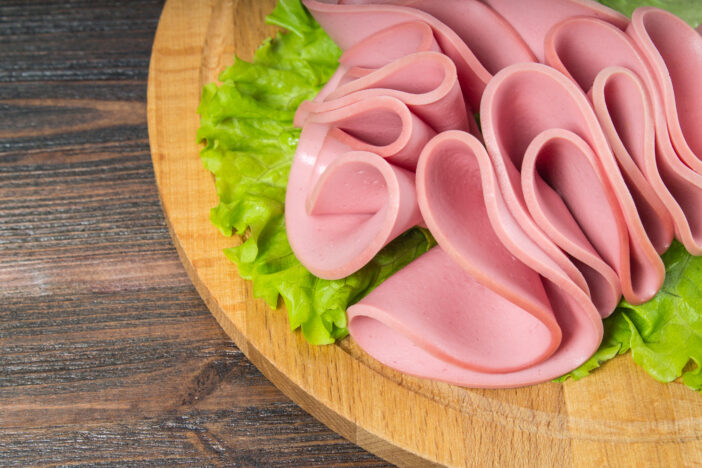 Sliced sausages with salad leaves on the wood background.