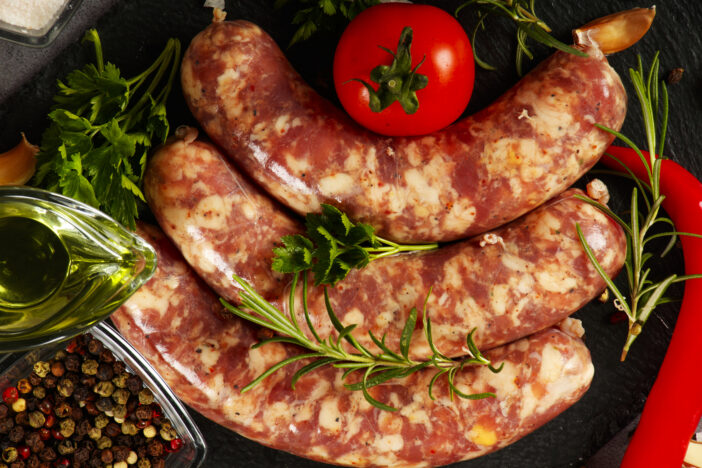 Bratwurst or sausages with spices and greens on a cutting board. On a  wooden table.