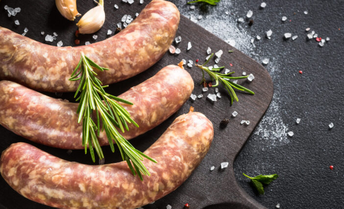 Bratwurst or sausages on cutting board with spices at black table. Top view with copy space.