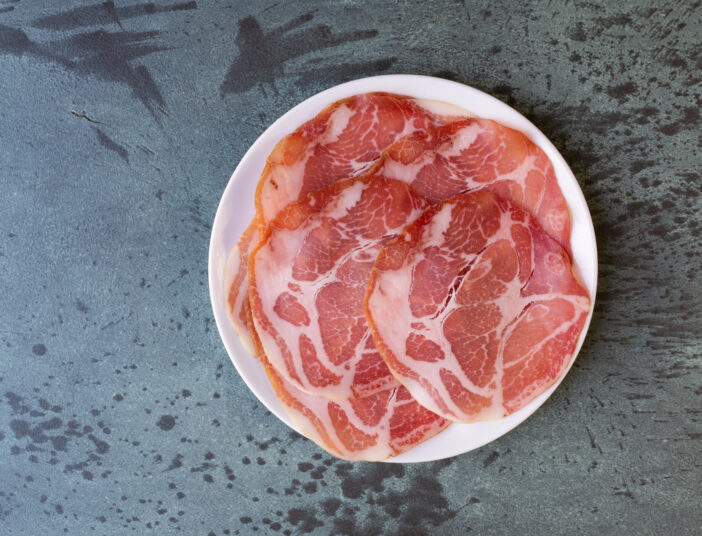 Overhead view of a plate of dry coppa on a gray mottled countertop illuminated with natural light.