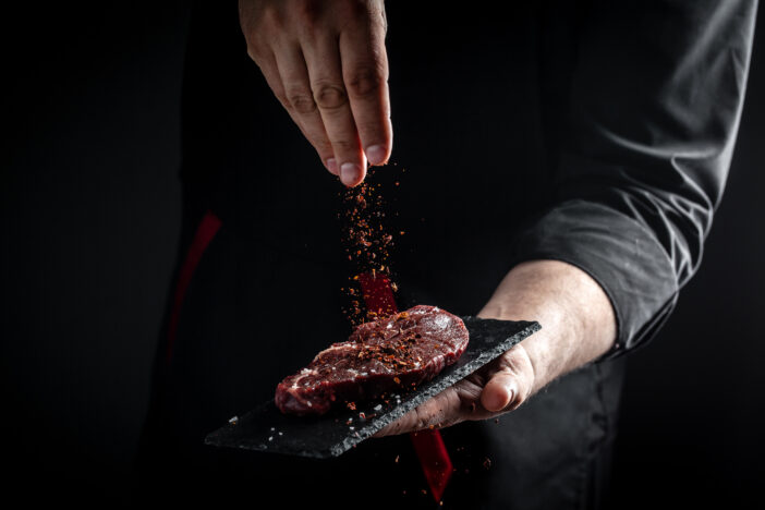 Chef hands cooking meat steak and adding seasoning in a freeze motion. Fresh raw Prime Black Angus beef rump steak. banner, menu recipe.