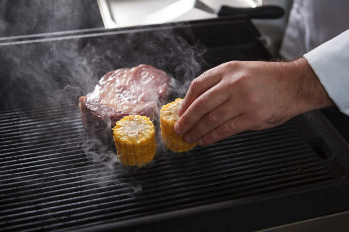 Chef putting sweet corn and beef steak on grill