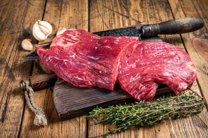 Flank raw beef steaks on a butcher cutting board with knife. wooden background. Top view.