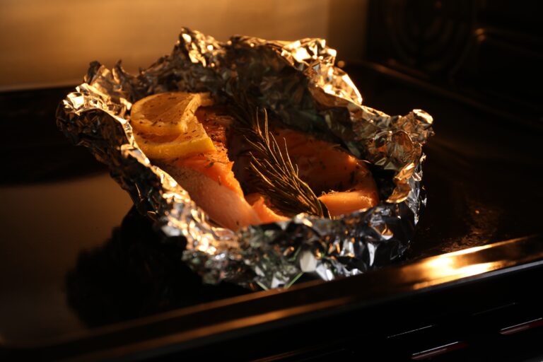 Foil with fish in oven, closeup. Baking salmon