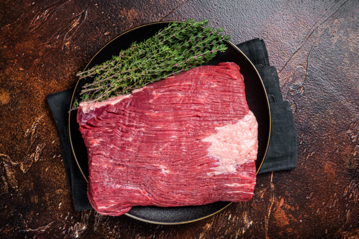 Fresh beef brisket, raw meat with herbs. Dark background. Top view.