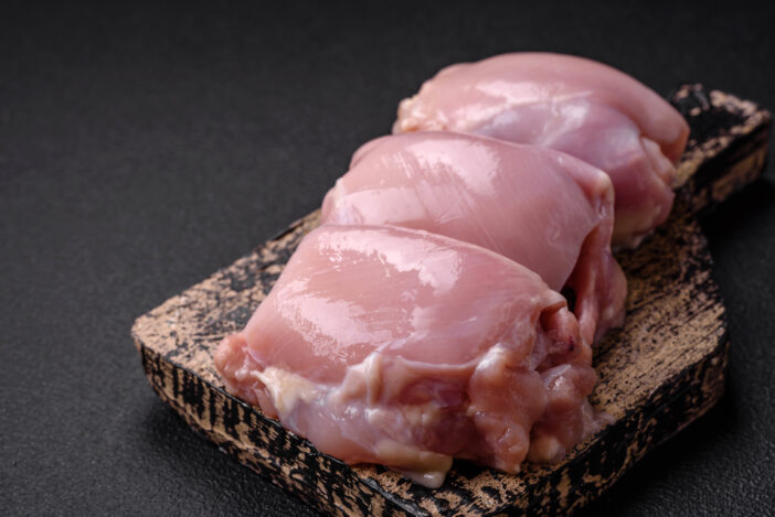 Fresh raw chicken thigh fillets with salt, spices and herbs on a dark concrete background