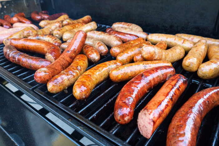 Fresh sausage and hot dogs grilling outdoors on a gas barbeque grill.