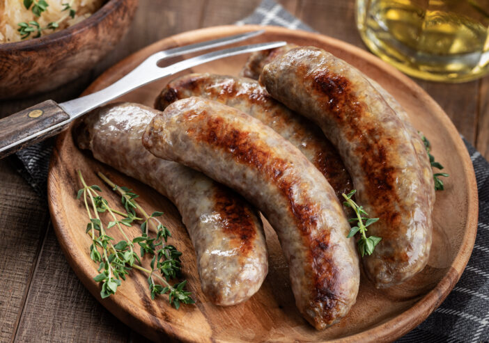 Fried bratwurst garnished with thyme on a plate on a rustic wooden table