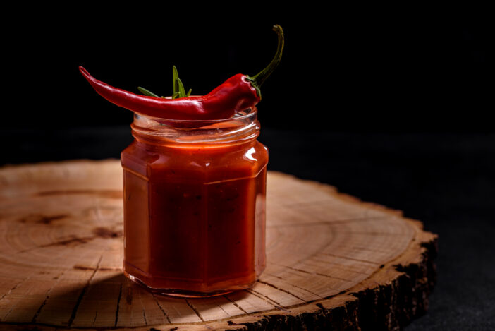 Glass jar with homemade classic spicy tomato pasta or pizza sauce with spices and herbs. Italian healthy food background