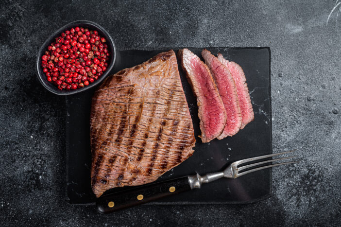 Grilled Flank Steak BBQ on a marble board. Black background. Top view.