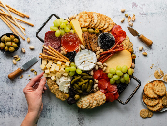 Hand sampling charcuterie board of meat, cheese, fruit, crackers. in Kingston, Ontario, Canada