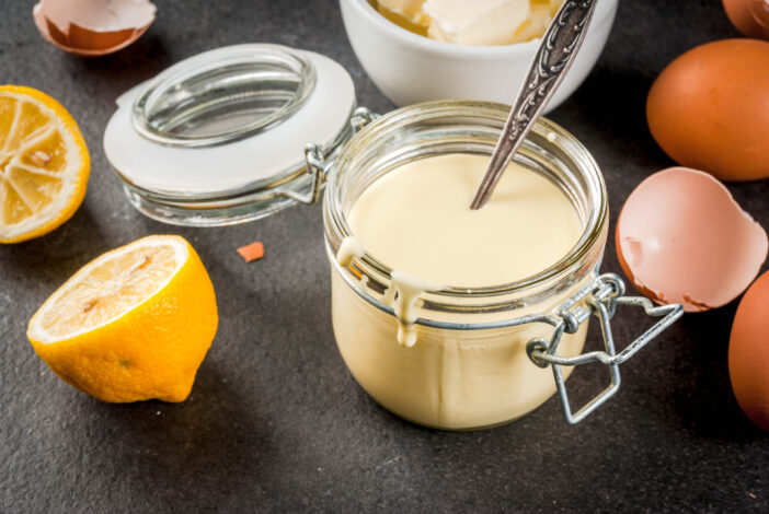 Traditional basic sauces. French cuisine. Hollandaise sauce in glass jar, with ingredients for cooking - eggs, butter, lemons. On a black stone table. Copy space