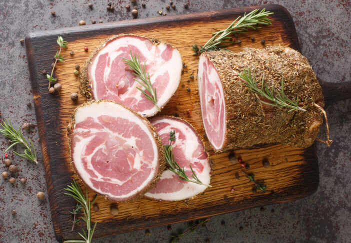 Italian traditional bacon pancetta on a cutting board closeup on the table. Horizontal top view from above