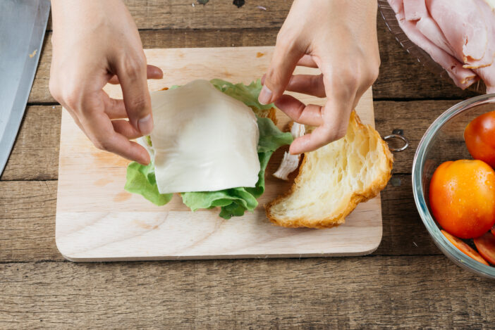 Making croissant sandwich, woman's hand placing cheese on croissant sandwich