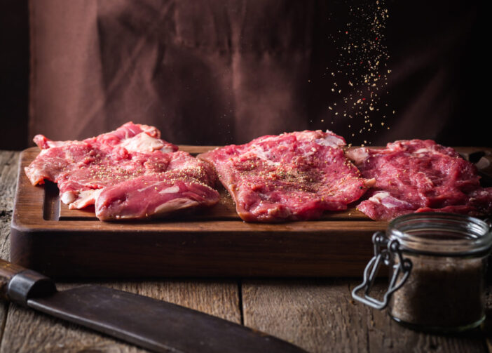 Man cooking meat steaks on kitchen. Chef salt and pepper meat on wooden background