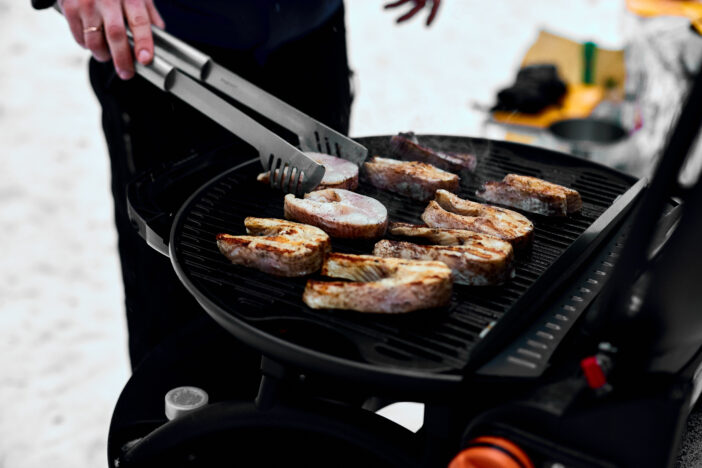 Man grilling delicious fish on a portable BBQ, Snowy winter barbecue outdoors in the cold . Outdoors winter barbecue party