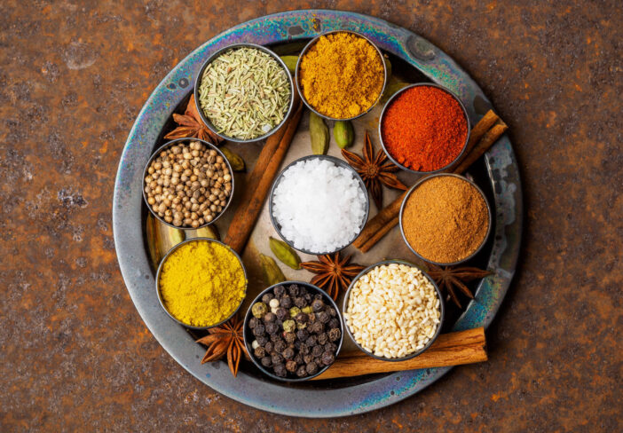 Mix spices on round metal plate - coriander seeds, ground red pepper, salt, black pepper, rosemary, turmeric, curry. Top view, close up, metall rusty background.