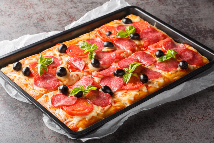 Italian fast food rectangular pizza with mozzarella, salami sausage, olives and tomatoes close-up in a baking sheet on the table. horizontal