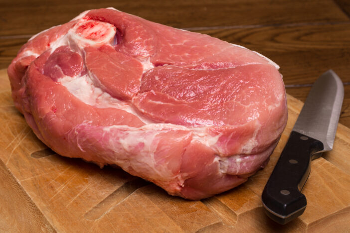 Raw cut of pork shoulder on cutting board with knife