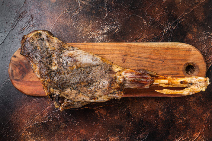 Roast lamb leg meat with herbs and spices on a cutting board. Dark background. Top view.