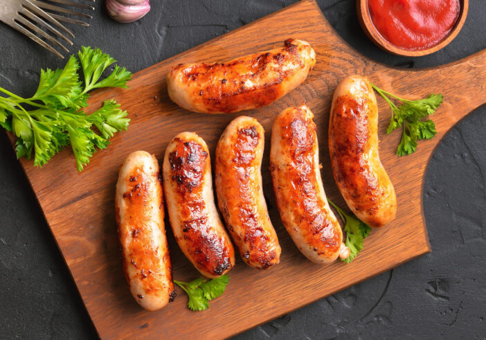 Roasted sausages on cutting board over dark background. Top view, flat lay