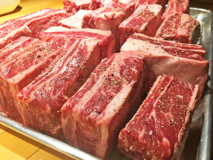 Seasoned raw beef short ribs on a baking pan ready to put into the oven.