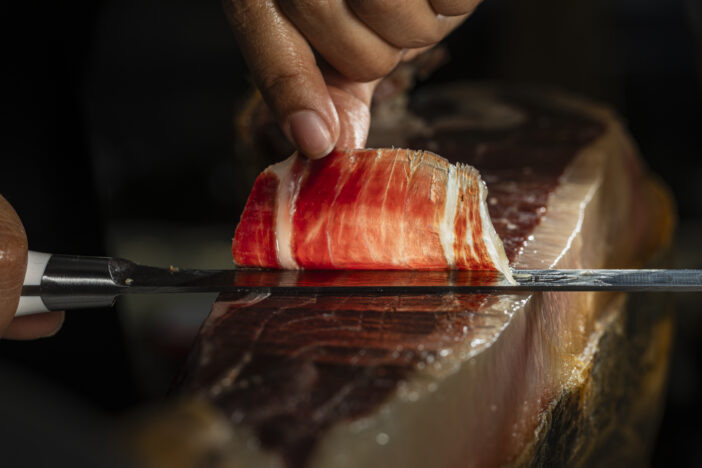 Slice of Iberian ham from Spain 100% acorn-fed, cut with a knife by a professional. Close up view of ham cutter typical of Spain gourmet product international sale