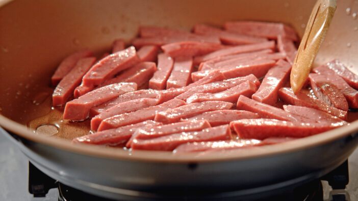 Sliced salami being thrown into a pan.