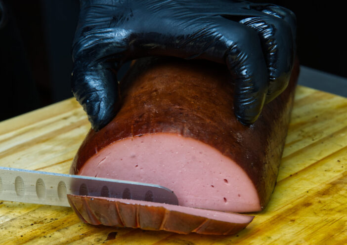 Slicing smoked bologna with a knife on a butcher's block.