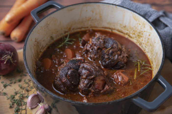 Slow cooked braised lamb shanks in crock pot or large casserole  with rosemary, thyme, onion, carrots