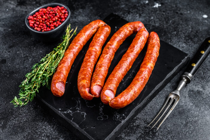 Smoked sausages on a marble board. Black background. Top view.