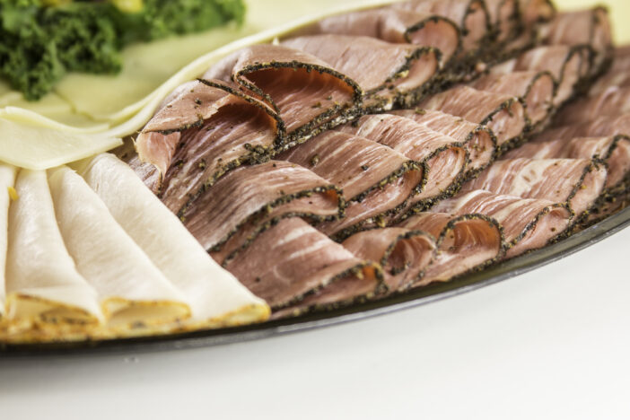 Thinly sliced deli pastrami and turkey folded and arranged and garnished on a catering tray