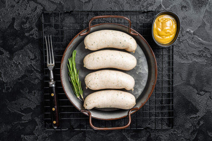 Traditional German Bavarian white sausage in steel tray with mustard. Black background. Top view.